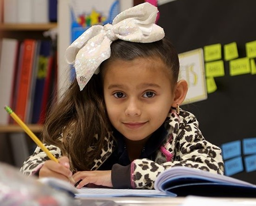 Student writing in notebook holding a pencil in her hand