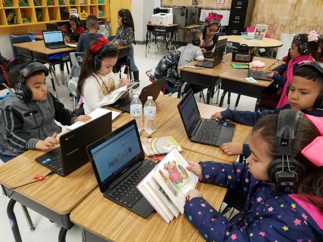 Students using technology and a following along with a book Students using technology and a following along with a book