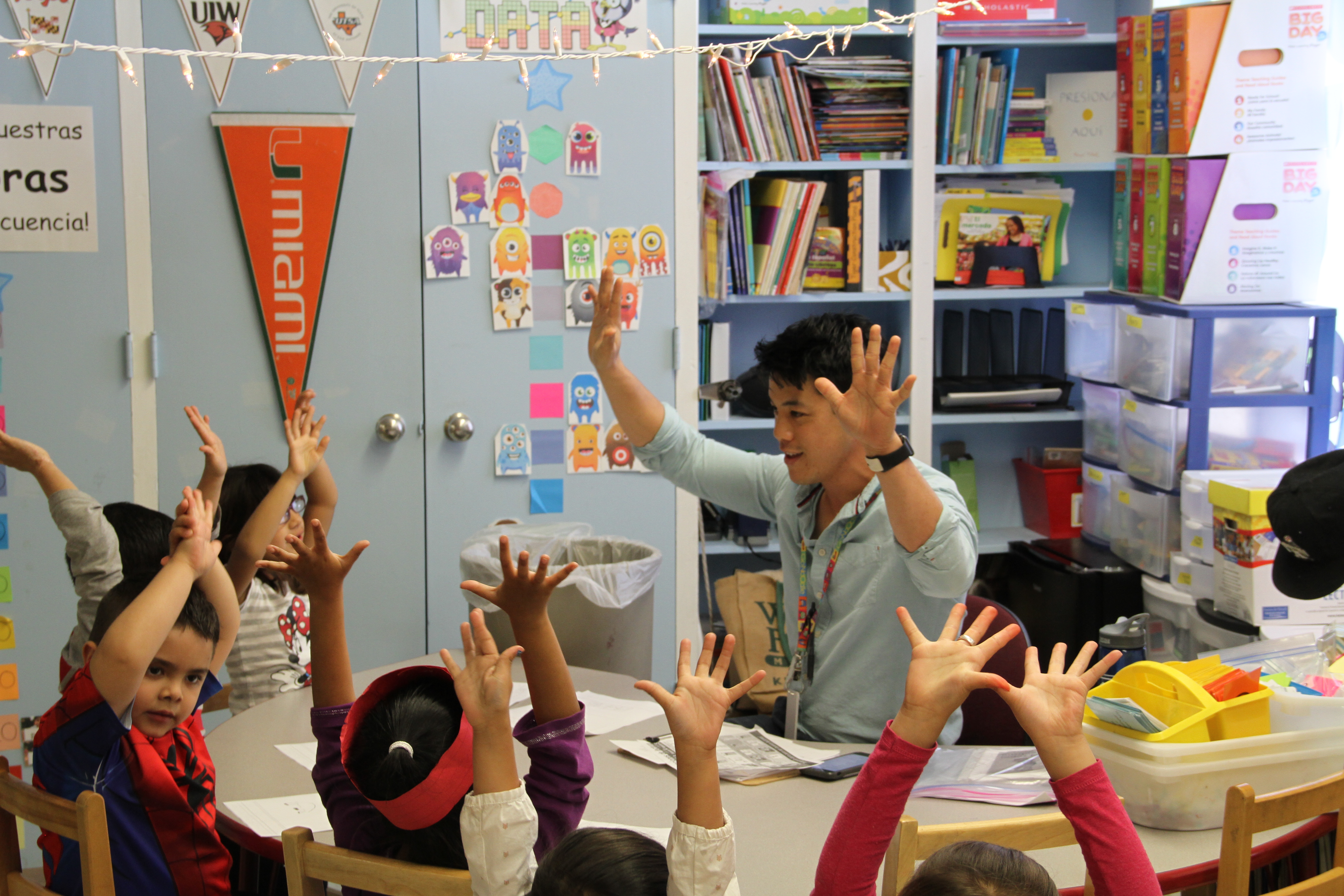 Teacher and elementary students raising both hands in the air in a classroom Teacher and elementary students raising both hands in the air in a classroom